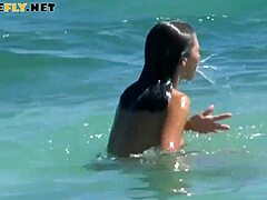 Katso topless-nudistien rannalla istuvan aurinkovoidetta