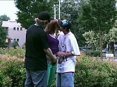 Twee mannen neuken een jong blond meisje in het openbaar terwijl auto's en vrachtwagens kijken in deze groepsseksvideo